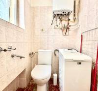 Fürdőszoba egy kétszobás lakásban WC-vel, mosógéppel és falra szerelt gázkazánnal.