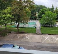 Kilátás egy háromszobás lakásból Pozsonyban - Ružinovban, a Mesačná utcában, parkoló, fák és játszótér.