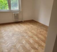 Szoba egy háromszobás lakásban, fa parkettával, nagy ablakkal, alatta radiátorral.