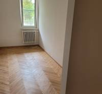 Szoba egy háromszobás lakásban, fa padlóval és radiátorral az ablak alatt.