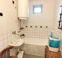 Családi ház fürdőszobája káddal, mosdóval, mosógéppel és vízmelegítővel.