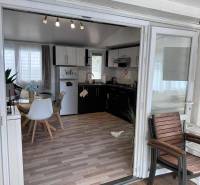 Belső tér világos asztallal, székekkel, konyhapulttal és fa dekorációjú padlóval.