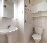 Fürdőszoba egy háromszobás lakásban mosdóval és WC-vel, világos csempékkel és tárolószekrényekkel.
