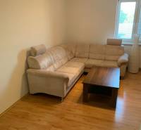 Nappali egy kétszobás lakásban sarokkanapéval és fa mintázatú padlóval.