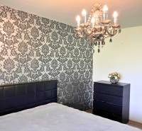 Hálószoba csillárral és tapétás fallal egy családi házban. Fa dekoros padló.