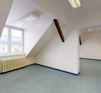 Tetőtéri irodák fehér falakkal, radiátorral és zöld szőnyeggel.