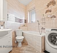 Fürdőszoba egy kétszobás lakásban mosógéppel, káddal, mosdóval és csempézett falakkal.