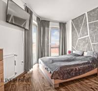 Hálószoba egy kétszobás lakásban, televízióval, ággyal és fa dekorációjú padlóval.