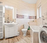 Fürdőszoba zuhanyzóval, káddal és mosógéppel egy kétszobás lakásban, fa hatású padlóval.