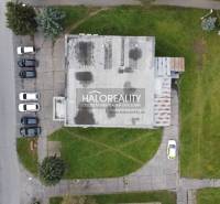 Kilátás Rimavská Sobota üzlethelyiségeire, amelyeket zöldterület és parkoló autók vesznek körül.