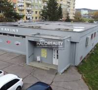 Egy üzlethelyiség épülete Rimaszombatban, panelházakkal és parkoló autókkal körülvéve.