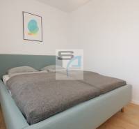 Hálószoba ággyal és minimalista dekorációval egy kétszobás lakásban, fa mintázatú padlóval.