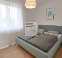 Hálószoba nagy ággyal, függönyökkel és fa dekorációjú padlóval egy kétszobás lakásban.