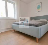 Hálószoba egy kétszobás lakásban, világos ágy, fa dekor padló, egyszerű dekoráció.