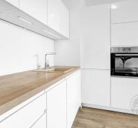 Konyhapult fa dekorációval, fehér szekrények és beépített sütő egy kétszobás lakásban.