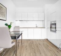 Konyha egy kétszobás lakásban fehér konyhabútorral, étkezőasztallal és fa mintázatú padlóval.