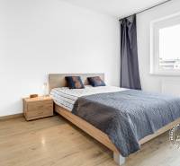 Hálószoba szürke ágytakaróval, fa szekrénnyel és fapadlóval egy kétszobás lakásban.