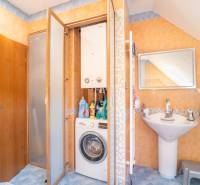 Fürdőszoba egy két szobás lakásban mosógéppel, gázkazánnal és mosdóval.