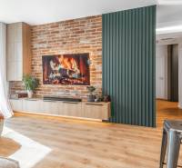 Nappali egy háromszobás lakásban téglafallal, kandallóval és fa mintázatú padlóval.