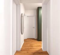 Keskeny belső tér fa dekor padlóval és egyszerű fehér fallal egy háromszobás lakásban.