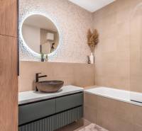 Fürdőszoba egy háromszobás lakásban mintás fallal, kerek tükörrel és káddal.