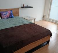 Hálószoba egy egyszobás lakásban fa dekor padlóval, ággyal és irodai székkel.