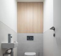 WC kerámia mosdóval, szürke csempével és fa mintázatú padlóval egy háromszobás lakásban.