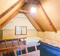 Podkrovás szoba egy faházban tetőgerendákkal és egyszerű bútorokkal.