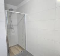 Zuhanykabin a családi ház fürdőszobájában csempével és fehér burkolattal.