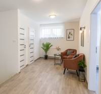 Családi ház belső tere fa dekorációjú padlóval, kényelmes fotelekkel és növényekkel.