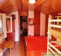 A kunyhó belseje emeletes ággyal, fa dekoros padlóval és nyitott ablakkal.