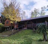 Házikó Dudincon, természet által körülvéve, terasszal és fákkal az udvaron.