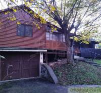 Faház Dudincon, fákkal és füves domboldallal körülvéve.