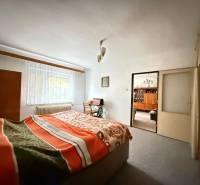 Hálószoba családi házban világos szőnyeggel, ablakkal és takaróval ellátott ággyal.