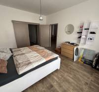 Hálószoba egy kétszobás lakásban fa mintázatú padlóval, ággyal és tárolóhellyel.