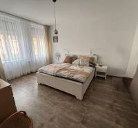 Hálószoba egy kétszobás lakásban nagy ablakokkal, ággyal és fa dekorációjú padlóval.