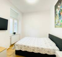 Hálószoba televízióval, ággyal és absztrakt festménnyel egy kétszobás lakásban.