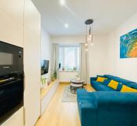 Nappali kék kanapéval, színes festménnyel és fa dekorációjú padlóval egy kétszobás lakásban.