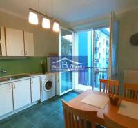 Konyha egy kétszobás lakásban fehér szekrényekkel, étkezőasztallal és erkéllyel.