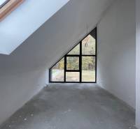 Tetőtéri szoba nagy ablakokkal és kiemelt mennyezettel egy családi házban, padlóburkolat nélkül.