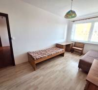 Egy szoba egy háromszobás lakásban, fa dekor padlóval, alap bútorokkal és nagy ablakkal.