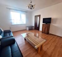 Nappali kanapéval, asztallal és televízióval, fa dekorációjú padlóval egy háromszobás lakásban.