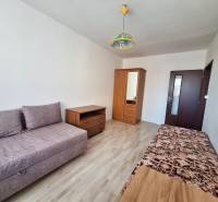 Nappali egy háromszobás lakásban, fa dekor padlóval és egyszerű bútorokkal.