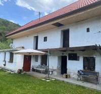 Vidéki ház piros tetővel és terasszal, zöld gyep és természet veszi körül.