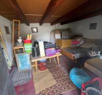 Egy használaton kívüli kunyhó belseje vidéki bútorokkal és mennyezeti gerendákkal.