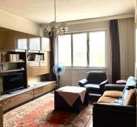 Nappali egy háromszobás lakásban bútorokkal, szőnyeggel és nagy ablakkal.