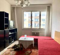 Nappali egy háromszobás lakásban piros kanapéval, szőnyeggel, régebbi televízióval, világos térrel.