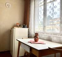 Ebédlő egy háromszobás lakásban asztallal, székekkel és virágmintás függönyökkel.