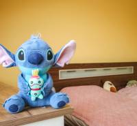 Egy szoba egy négy szobás lakásban sárga falakkal, játékokkal és egy ággyal rózsaszín ágytakaróval.