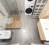 Fürdőszoba mosógéppel és zuhanyzóval egy 4 szobás lakásban, fa dekor padlóval.